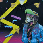 Close-up of a black lace-up jersey featuring a retro 80s graphic of a skeleton in shutter shades and a blue jacket, surrounded by colorful Memphis-style geometric shapes.