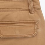 Close-up of a tan twill garment showing a pocket flap, belt loop, and detailed stitching.