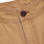 Close-up view of the waistband of tan twill pants, featuring a dark brown button and detailed double stitching.