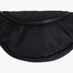 Close-up of a black crescent-shaped nylon waist bag with a chunky black zipper on a white background.