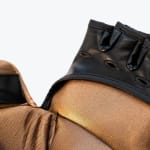 A close-up view of a glove featuring a textured gold ribbed fabric and a black leather trim with decorative cutouts.