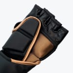 Close-up of a black fingerless MMA glove with gold trim and a ribbed bronze elastic section on a white background.