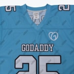 Close-up of a light blue GoDaddy jersey with white and black lettering, a heart logo, and shoulder numbers.