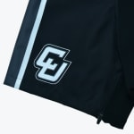 Close-up of black athletic shorts showing a vertical white side stripe, a white interlocking EG logo, and a small zipper on the hem.