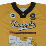 A yellow baseball jersey with black collar trim, featuring the cursive Doggett logo, an Astros sponsor logo, and a map of the southern US states on the bottom.