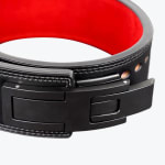 Close-up of a black leather powerlifting belt with a matte black lever buckle and a bright red interior lining.