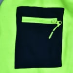 Close-up of a black rectangular pocket with a neon green zipper on a bright neon green fleece fabric.