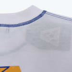 Close-up of a white t-shirt collar featuring blue contrast stitching and a faint inner tag visible through the fabric.