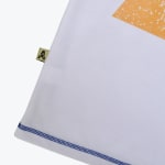 Close-up of a white t-shirt hem featuring blue contrast stitching, a small gold side tag with a star logo, and a portion of an orange graphic print.