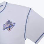 Close-up of a white t-shirt with blue contrast stitching and a diamond-shaped URBANO 2001 graphic logo on the chest.