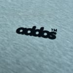 Close-up of a grey heather fabric with a black embroidered logo reading addos with a TM trademark symbol.
