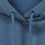 Close-up of a dusty blue hoodie showing the collar area, two eyelets, and braided drawstrings.