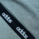 Close-up of grey heathered fabric with a diagonal black stripe featuring the white Addos logo printed repeatedly.