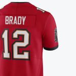 The back of a red Tampa Bay Buccaneers jersey showing BRADY and the number 12 in white with orange and black borders.