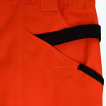 Close-up of bright orange work pants featuring a utility pocket with black tool straps and reinforced stitching.