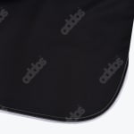 Close-up of black fabric with a subtle repeating adidas wordmark pattern and a rounded hem stitched in white.