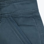 Close-up view of the front pocket and waistband of dark teal twill trousers, showing detailed stitching and fabric texture.