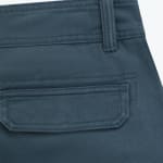 Close-up of a dark teal pant pocket with a stitched flap and a belt loop on twill fabric.