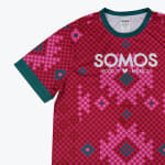 A close-up of a magenta checkered t-shirt with teal trim and the white text SOMOS FOOD FROM THE HEART OF MEXICO.