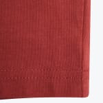 A close-up of a terracotta-colored knit fabric showing a double-stitched hem at the bottom and a vertical seam on the right.