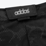Close-up of black patterned athletic shorts showing the addos brand logo on a waistband flap and a PERFORMANCEPRO+ tag.