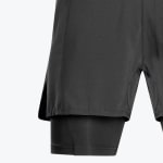 Close-up of black 2-in-1 running shorts showing the patterned outer layer and the inner liner with a side slit.