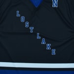 A close-up of a dark blue sports jersey with LOST LAKE written diagonally in blue block letters with white outlines.