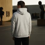 Back view of a man wearing a light grey speckled hoodie and black pants in an outdoor courtyard with sculptures.