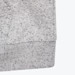 Close-up of a light grey heathered sweatshirt showing the ribbed bottom hem and a stitched pocket detail.