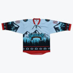A light blue, black, and red hockey jersey with the word 'GRIZZLIES' on the front, featuring mountain and forest graphics and Indigenous art patterns.