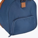 Close-up of a navy blue canvas duffel bag showing a zippered side pocket and a brown leather patch with a strap attachment.
