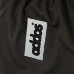 Close-up of a white rectangular patch with black addos text sewn onto dark folded fabric.