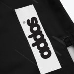 Close-up of a white rectangular patch with the word addos printed vertically in bold black letters on black fabric.