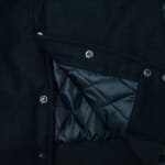 Close-up of a black wool jacket partially unbuttoned to show its shiny black diamond-quilted lining and metal snap buttons.