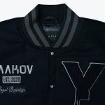A close-up shot of a black varsity jacket featuring a striped collar, a large embroidered letter Y, and text patches reading YAKOV, EST. 2020, and Royal Berkshire.