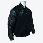 A black varsity jacket with leather sleeves, grey striped trim, and custom embroidery displayed on a mannequin.