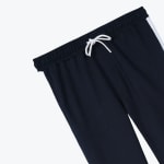 Close-up of navy blue sweatpants showing the elastic waistband, a white drawstring tied in a bow, and a white stripe on the side.