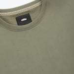Close-up of an olive green crew neck sweatshirt showing the ribbed collar, a black addos brand label, and a patterned inner neck tape.