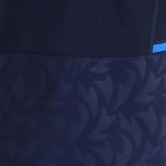 Close-up of dark navy blue athletic fabric with a horizontal flatlock seam separating a solid top section from a patterned bottom section featuring embossed curved shapes.