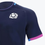 Close-up of a navy blue Scotland Rugby shirt showing the white thistle logo on the chest and pink and blue details on the collar and sleeve cuff.