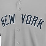 Close-up of a grey baseball jersey with NEW YORK in navy blue block letters outlined in white across the chest.