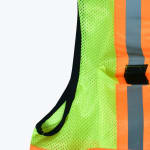 Close-up of a neon green and orange safety vest with reflective silver stripes and black trim.