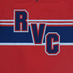 Close-up of a red athletic jersey with the letters RVC in bold blue, red, and white collegiate font over a blue horizontal stripe.