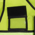 Close-up of a clear plastic ID badge holder with a black border and velcro flap on a lime-green mesh safety vest.
