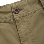 Close-up of olive green trousers showing the waistband, stitching details, and a brown button closure.