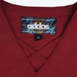 Close-up of a maroon scrub top neckline with an Addos Workwear Collection label and size M tag.