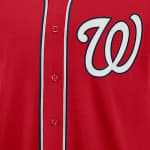 Close-up of a red Washington Nationals baseball jersey showing the white curly W logo and red buttons.