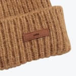 Close-up of a camel brown ribbed knit beanie with a small rectangular brown patch showing the addos logo.