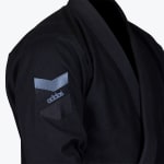 Close-up of the sleeve of a black Addos Jiu-Jitsu gi featuring a grey and black brand logo patch on the upper arm.