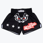 Black Muay Thai shorts with a central angry eyes graphic, three white stars on one leg, and red and white Thai script on the other leg.
